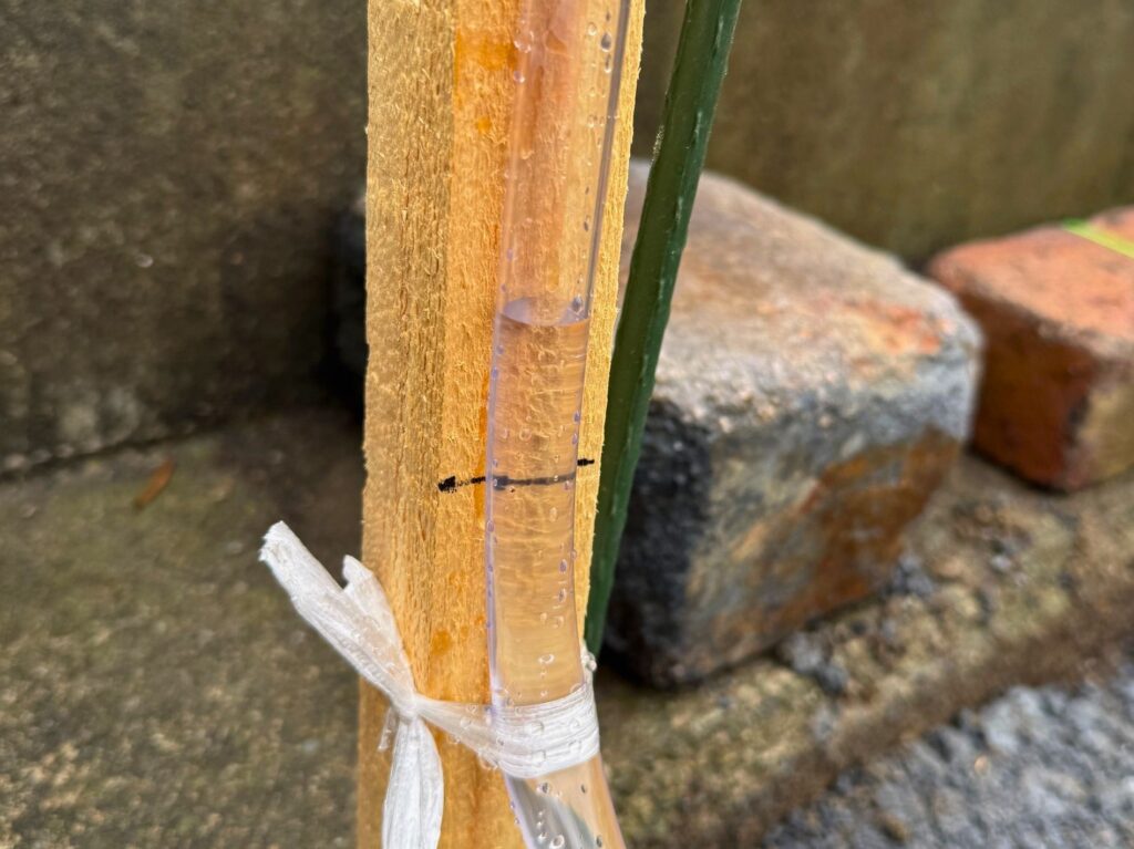水盛りで水平を出すために透明ホースの水位を基準にしている様子